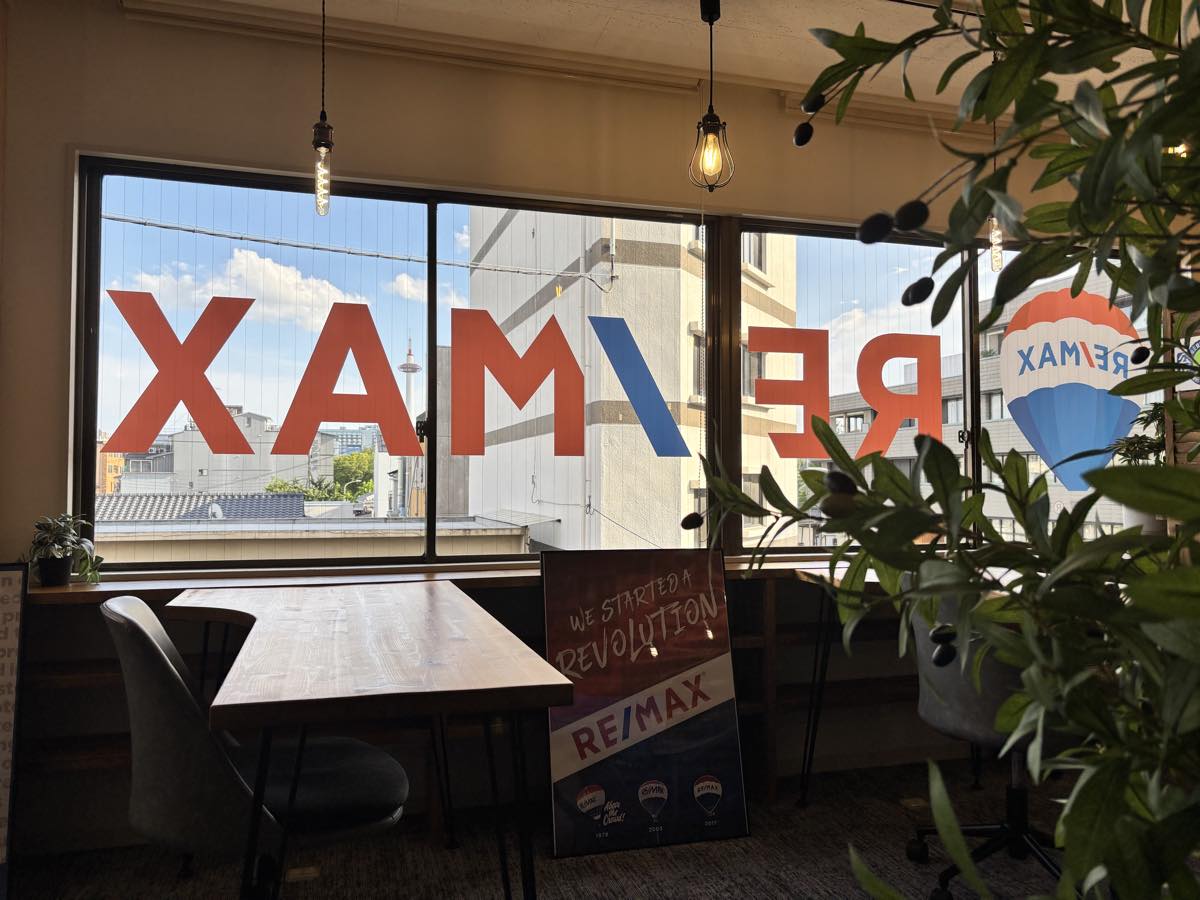 RE/MAX のサインが入った窓越しに京都タワーを望むワークスペース